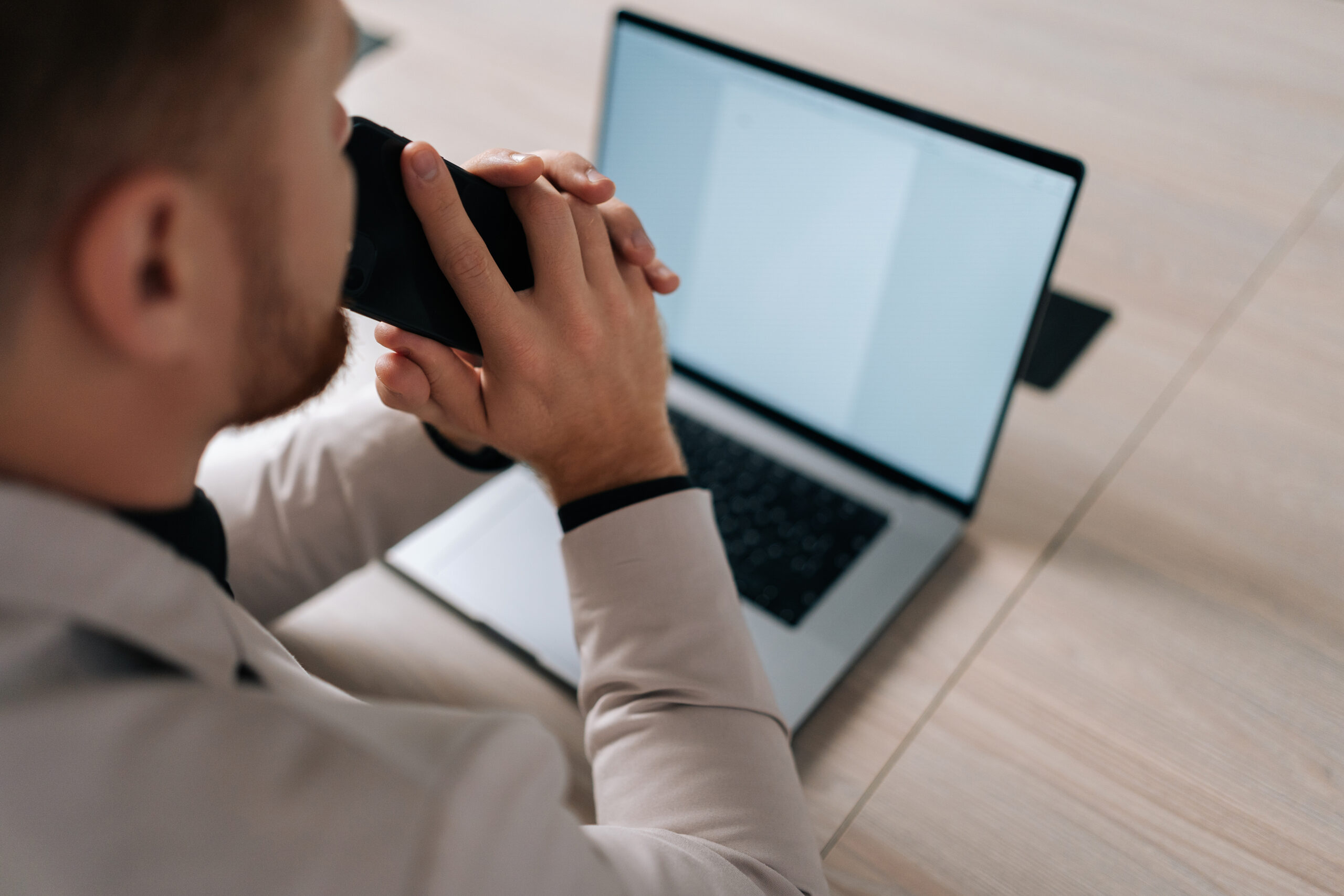 Un uomo è seduto davanti al suo laptop con uno schermo vuoto, tenendo un telefono cellulare all'orecchio, simboleggiando la comunicazione strategica necessaria per superare la bassa stagione nel settore dell'ospitalità. L'immagine cattura un momento di concentrazione e pianificazione, essenziale per elaborare strategie efficaci e migliorare le prestazioni aziendali durante i periodi meno affollati.